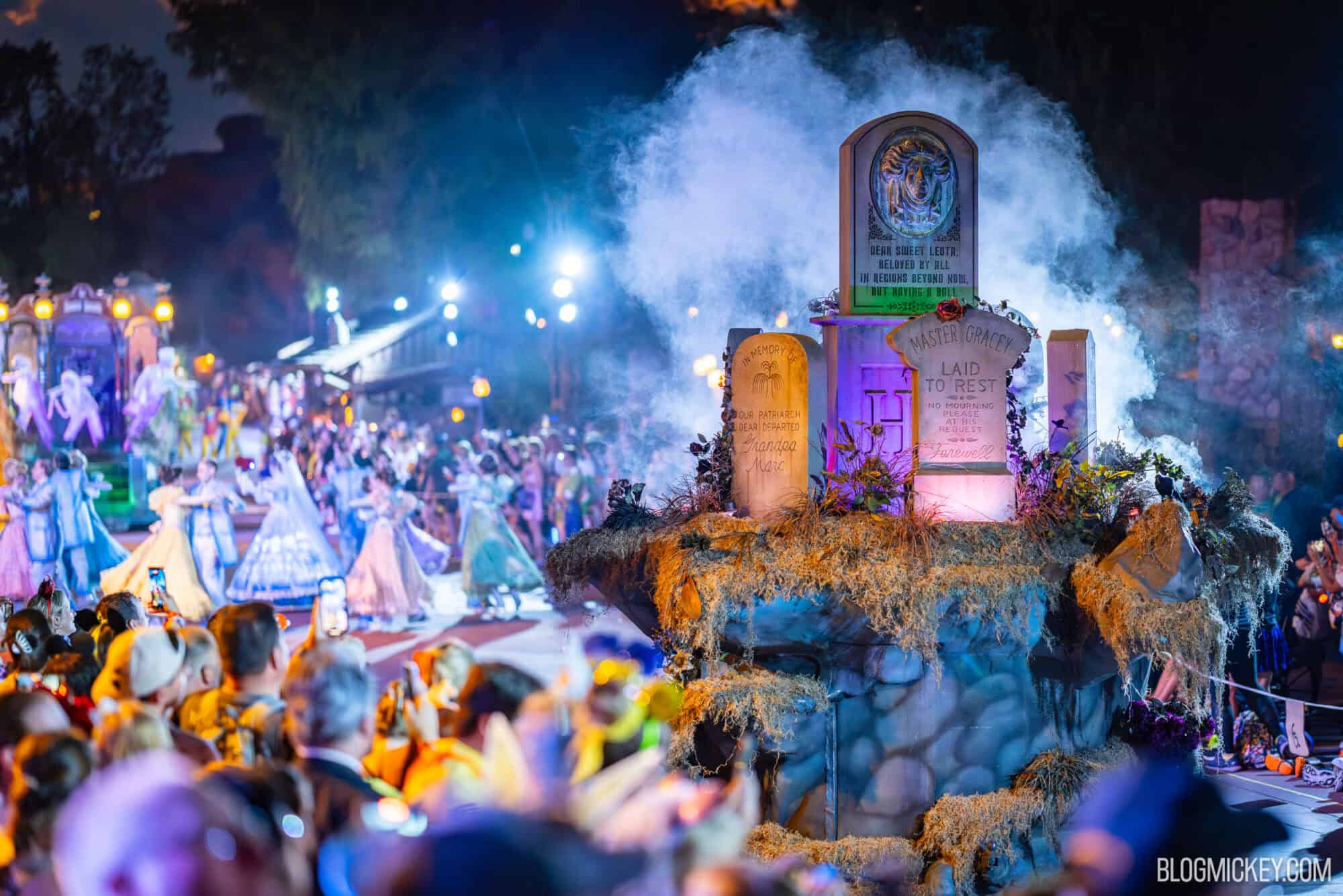 Colorful Disney Halloween parade at night with illuminated floats featuring tombstones and costumed characters.