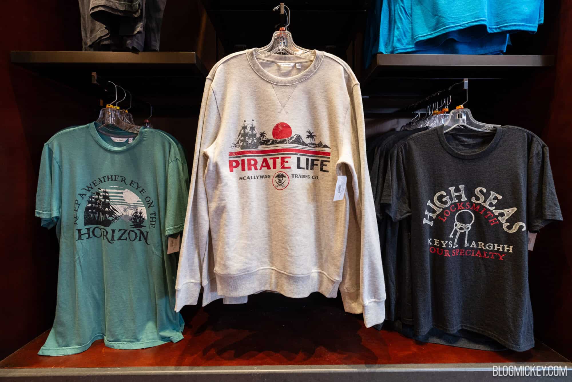 Men's and women's crewneck sweatshirts with pirate, nautical, and adventure-themed designs from Disney World merchandise displays. Perfect for Disney fans and gift shoppers.