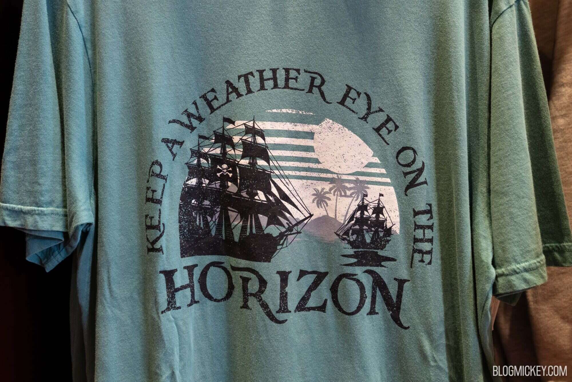 Vintage-style teal T-shirt featuring a graphic of sailing ships, palm trees, and the phrase "Keep an Eye on the Horizon," celebrating maritime adventure and tropical scenery.