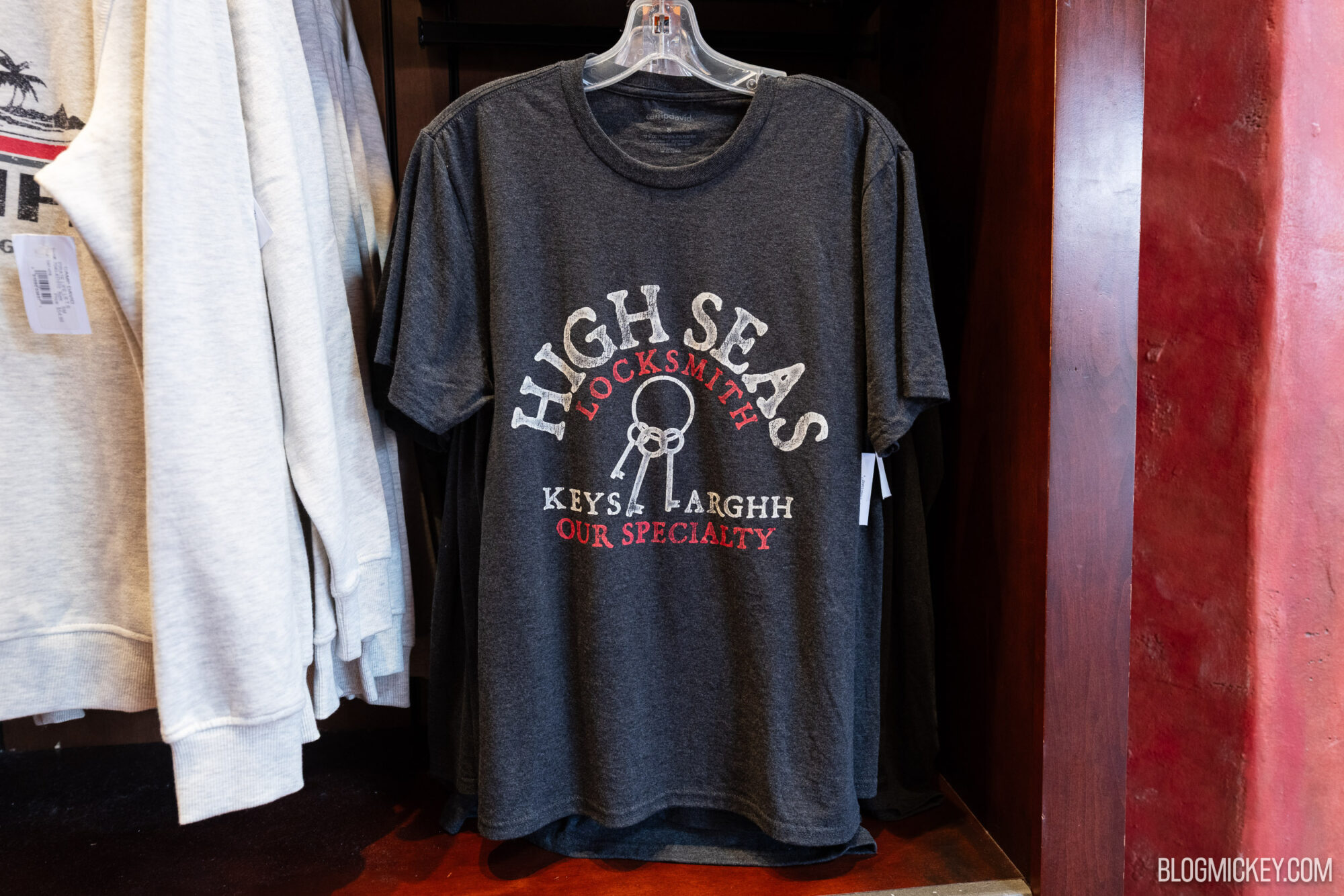 Black T-shirt with "High Seas Locksmith Our Specialty" graphic, featuring a key and nautical theme, displayed in a retail store.