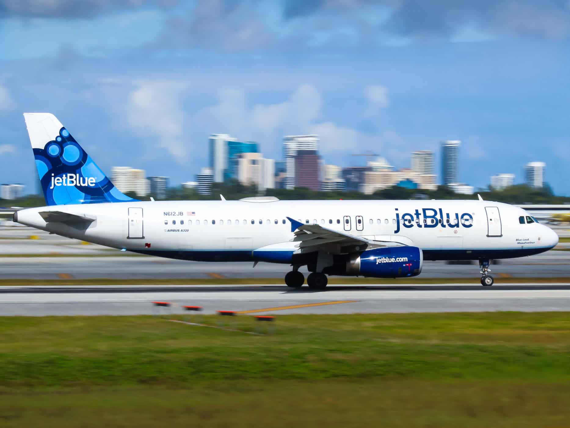 JetBlue airplane taxiing on runway with city skyline in background.